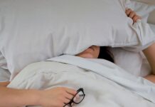 신체 회복과 면역력 증진 person lying on bed while covering face with pillow and holding eyeglasses